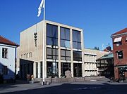 Stadshuset i modernistisk stil (funktionalistisk stil) vid Rådhustorget intill rådhuset (det blå huset som syns till vänster). Stadshuset uppfördes 1959 och ritades av Lennart Tham. På väggen vänster om flaggstången hänger stadshusets klockspel
