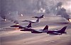 Kuwaitkriget bryter ut denna dag 1991: Amerikanska stridsflygplan av typerna F-16A, F-15C och F-15E flyger ovanför brinnande oljekällor i öknen.